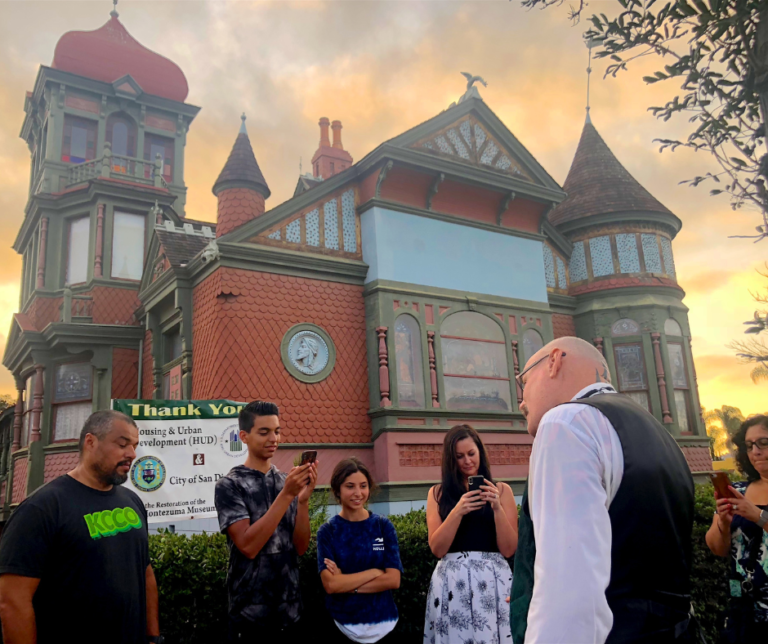 Image of Villa Montezuma, a Victorian-era mansion in San Diego, taken during a guided tour. Tour participants are visible on the front lawn.