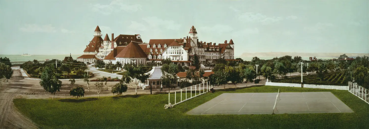 A hand-tinted photochrom print, circa 1900, of the Hotel del Coronado and its grounds, including an early tennis court, with no people visible.