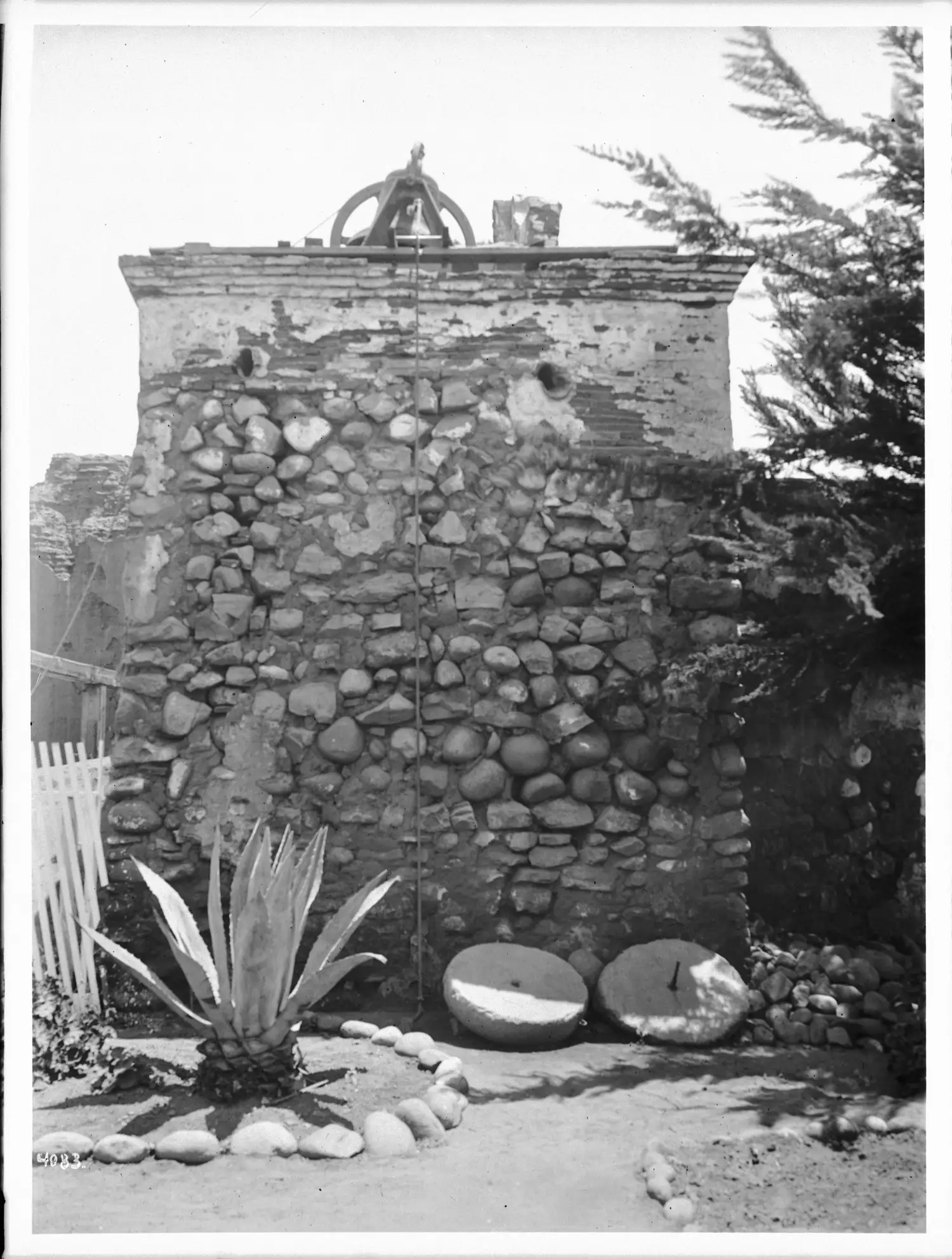 A circa-1905 photograph of the weathered stone bell tower at Mission San Diego de Alcalá, with an agave plant in the foreground.