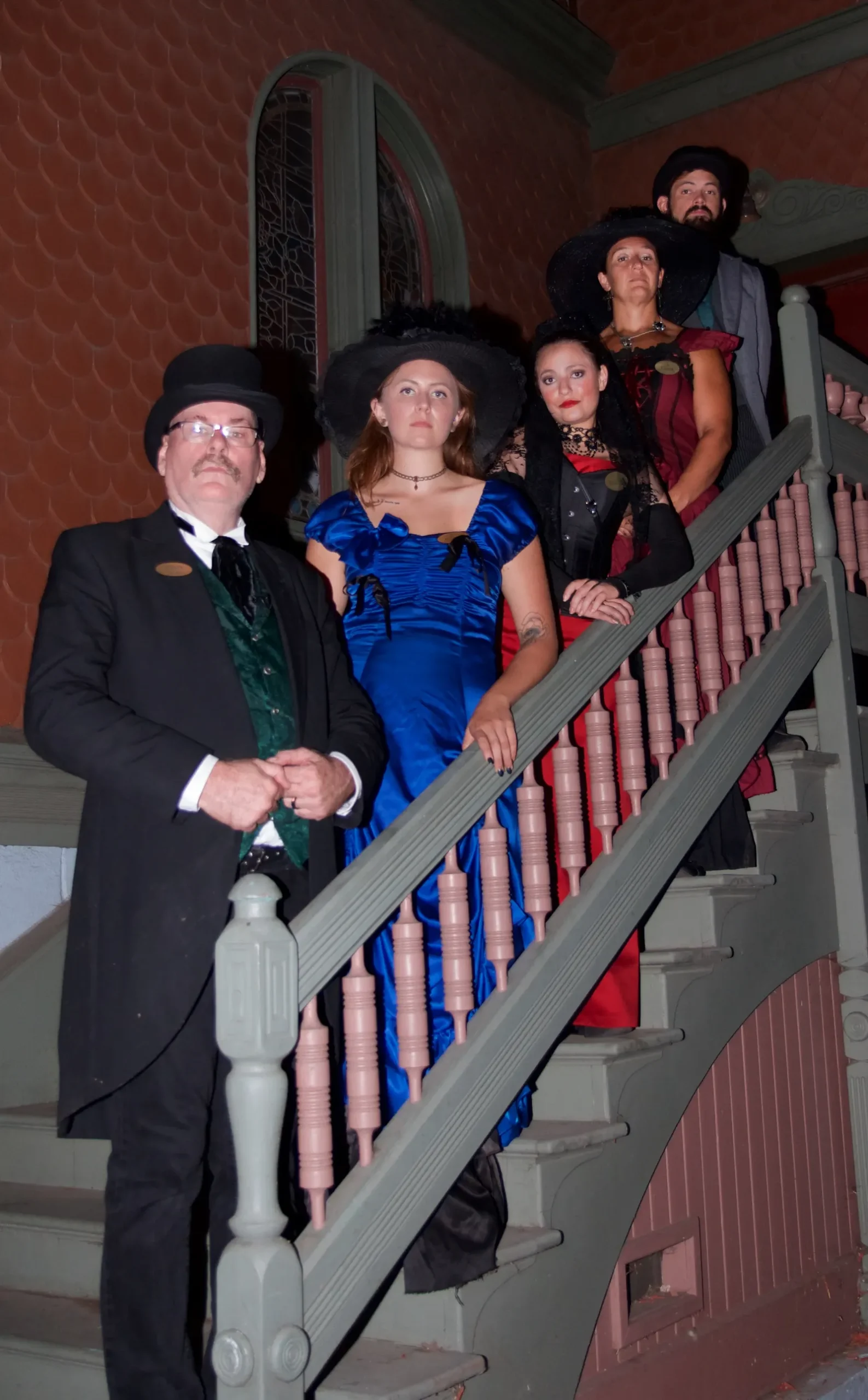 Five HSDGT guides in full Victorian-era costume stand together on an ornate wooden staircase inside a historic Old Town building.